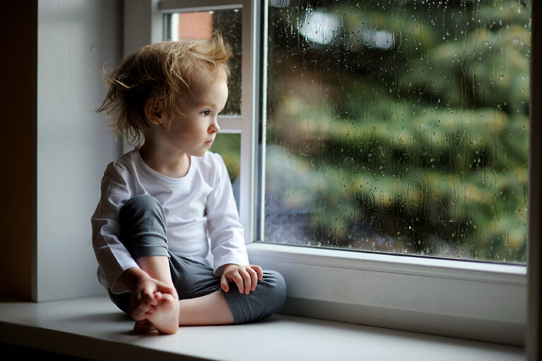 Menina criança olhando pela janela com olhar vazio.